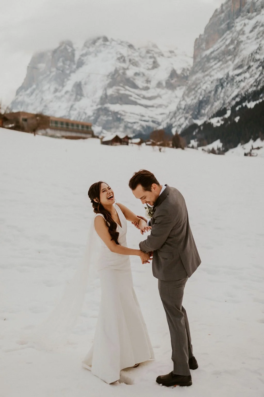 A happy bride and groom are holding hands and laughing in a snowy mountain landscape.