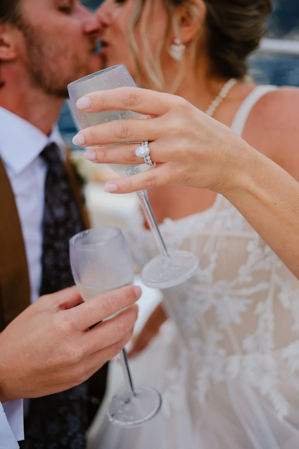 Close-up of a bride and groom sharing a kiss, holding champagne glasses during their wedding celebration.