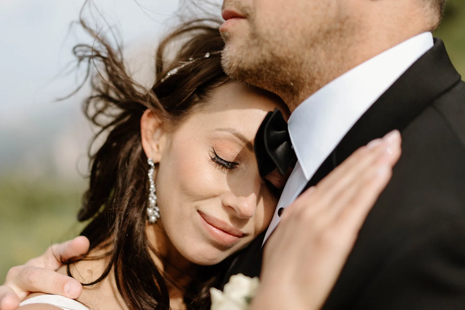 Close-up of a couple embracing, with the woman resting her head on the man's shoulder, eyes closed, both dressed elegantly for a formal occasion.