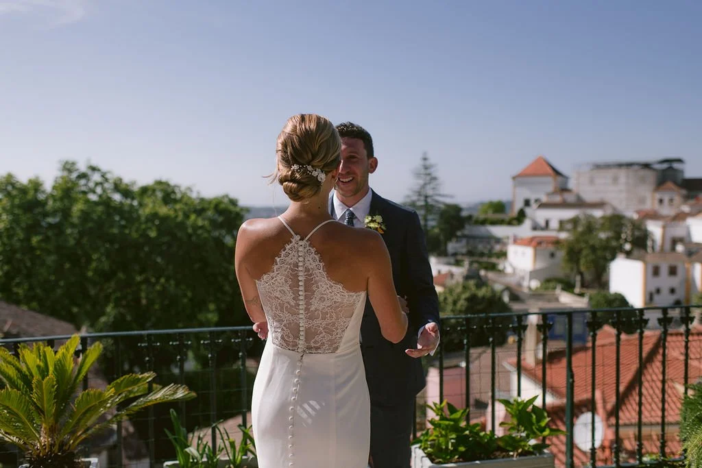 A bride and groom holding hands on a balcony with a cityscape in the background.