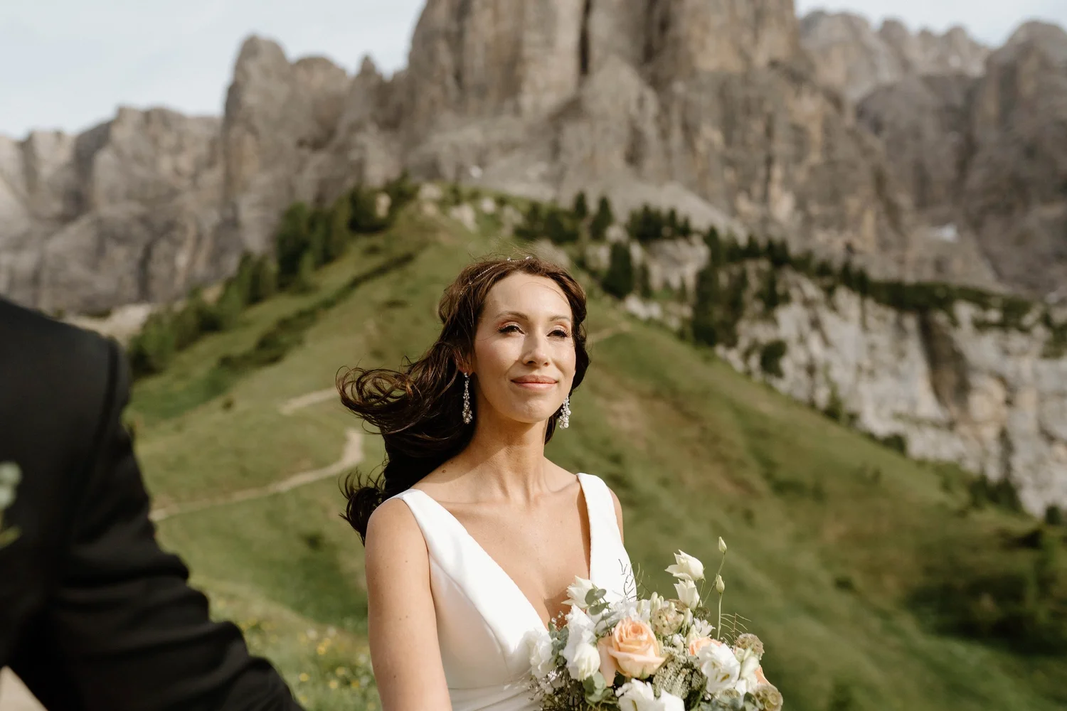 A woman in a white dress holding a bouquet of flowers outdoors with mountains in the background.