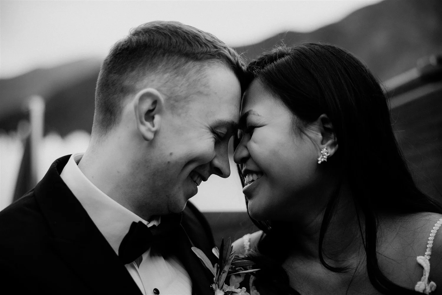 A black and white photograph of a couple with foreheads touching and eyes closed, smiling during what appears to be a wedding or special event.