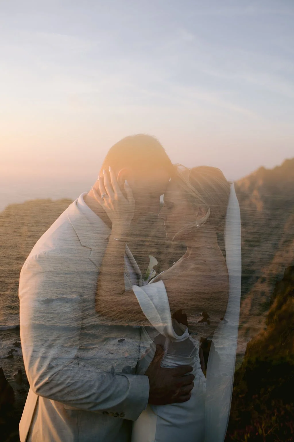 A romantic couple sharing a kiss on the beach at sunset, with the sunset and ocean reflected over the photograph.