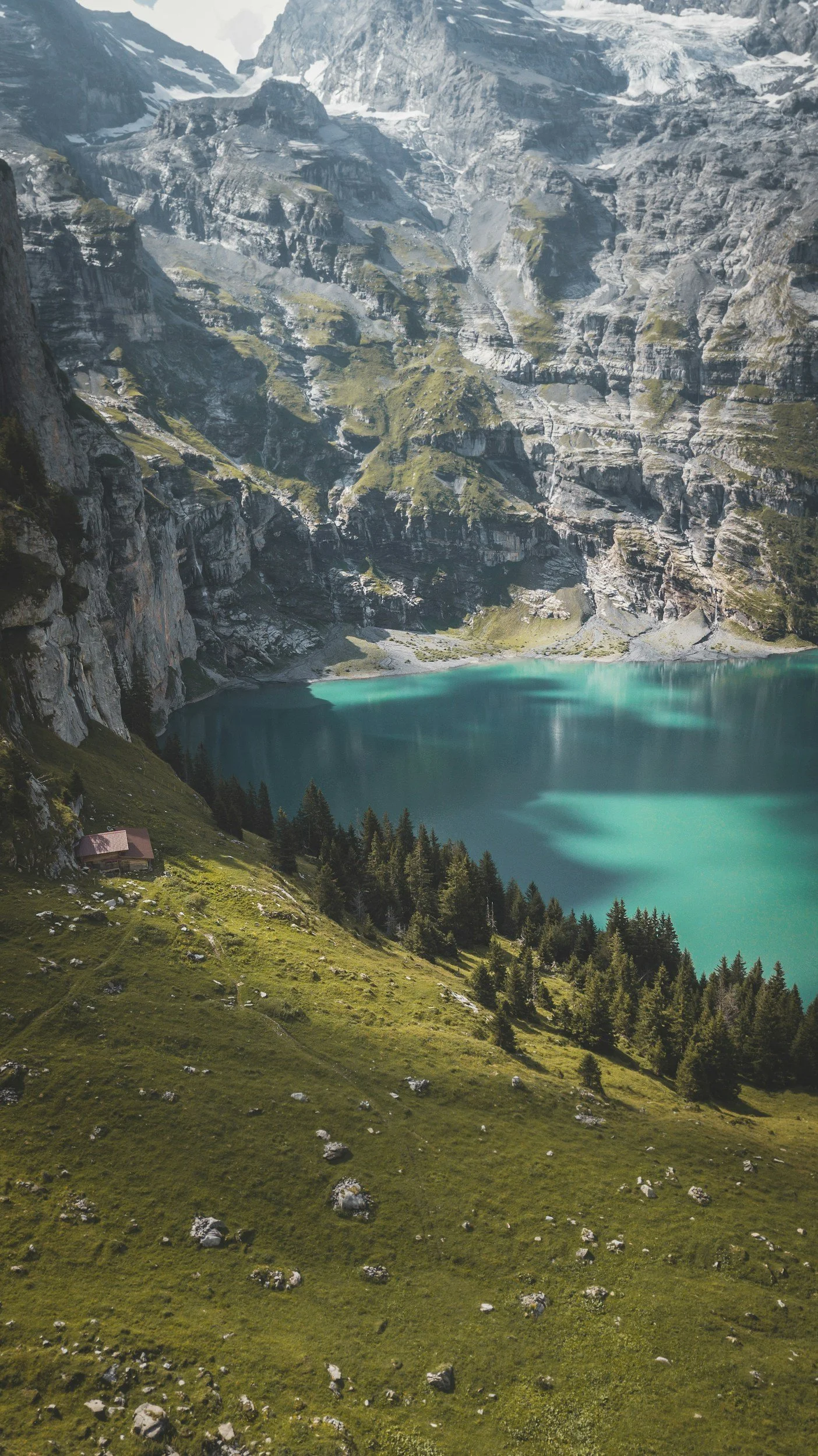 Scenic mountain landscape with a turquoise lake, rocky cliffs, and lush green trees and grass in the foreground.