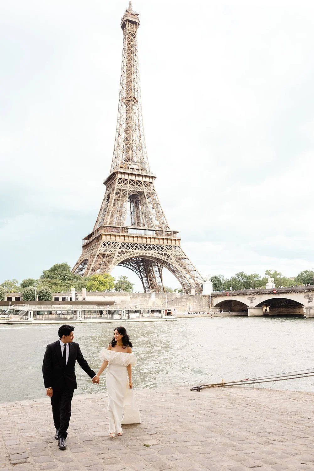 A couple holding hands walking along the Seine River with the Eiffel Tower in the background in Paris, France.