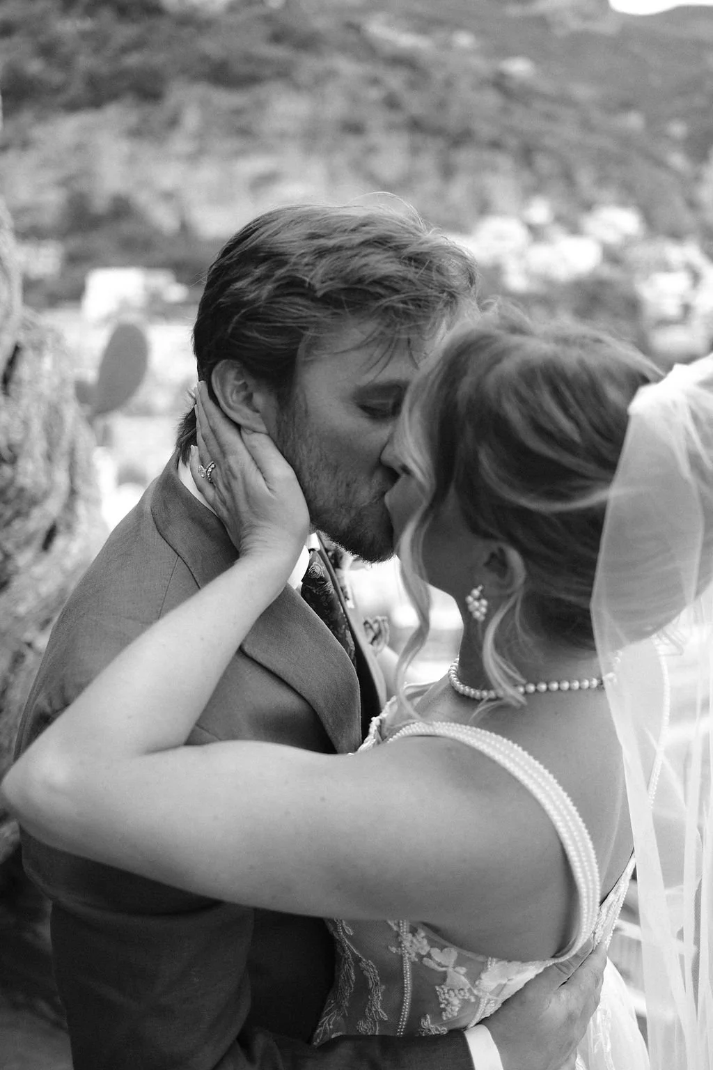 A black and white photo of a couple kissing, with their foreheads touching and arms wrapped around each other, on their wedding day.
