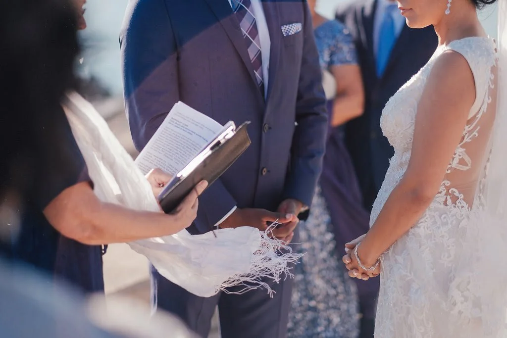 Bride and groom standing outdoors during their wedding ceremony, with the officiant holding a book.