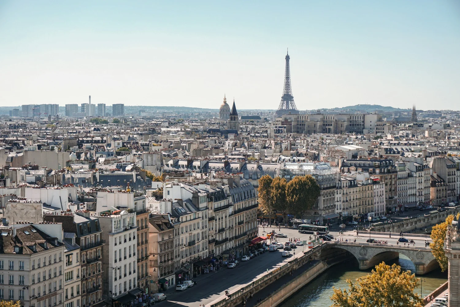 View of Paris cityscape with the Eiffel Tower in the background, surrounded by classic Parisian buildings, streets, and a river.