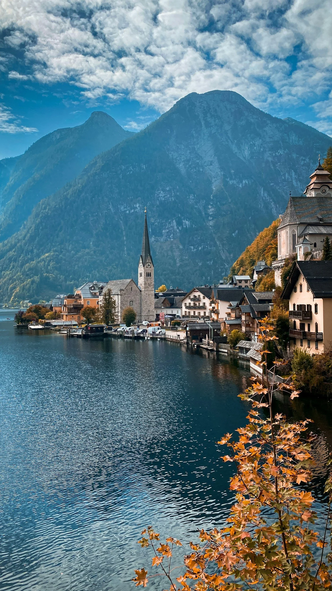 A lakeside village with a church and colorful buildings surrounded by mountains during autumn with fall foliage.