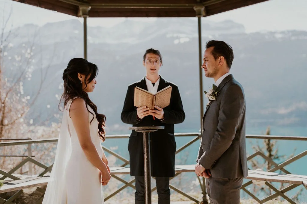 Couple getting married outdoors with officiant reading vows, scenic mountain background.