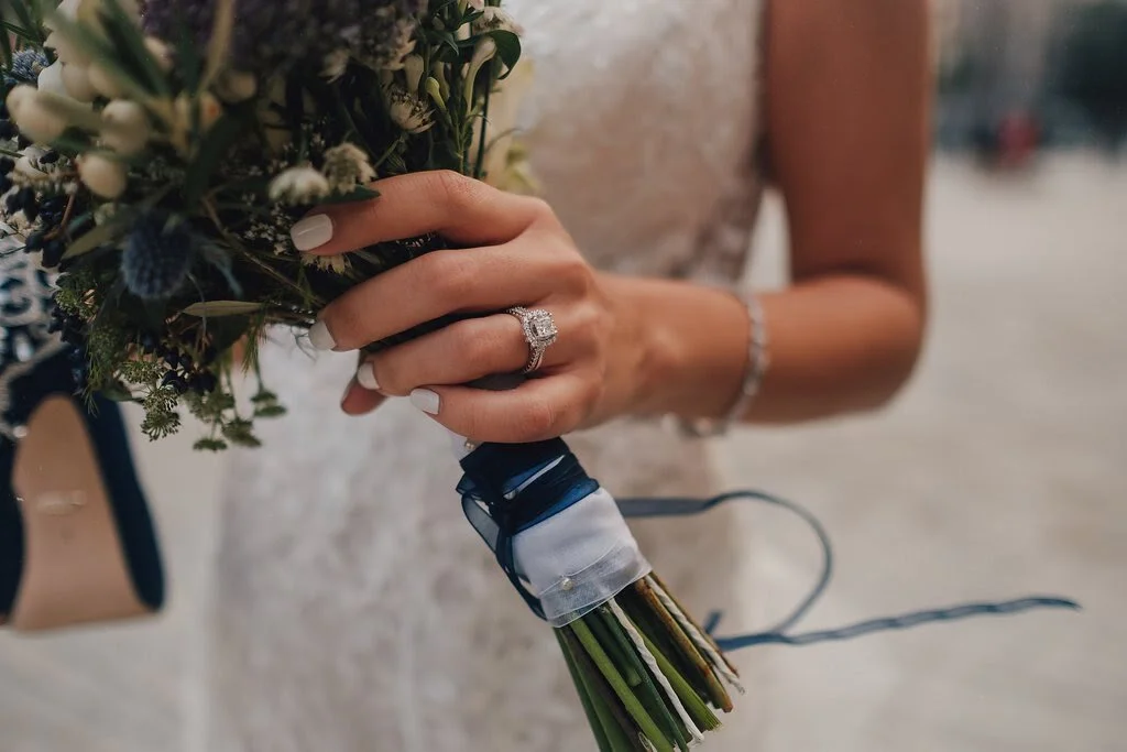 A woman wearing a wedding dress holding a bouquet of flowers and displaying an engagement ring on her finger.