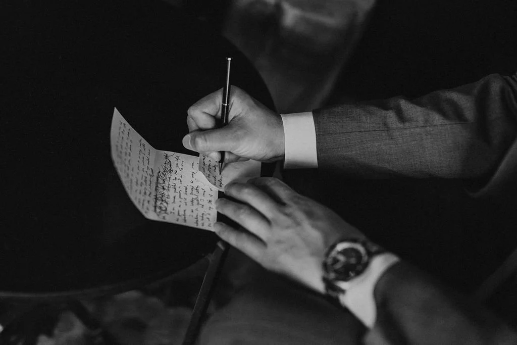 A person in a suit writing a handwritten letter on paper with a pen, sitting at a table.